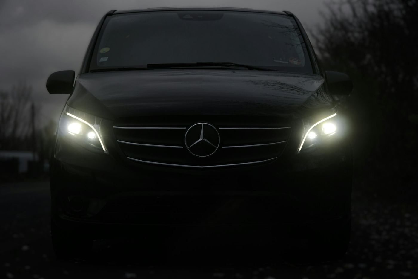 A black Mercedes van with headlights on